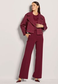 Bordeaux cropped jasje met dubbele knopen, gecombineerd met een bijpassende top en wijde broek. Glad textuur; hoge hakken maken de look compleet.