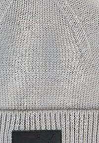 Gray knitted beanie with a ribbed cuff, featuring a black leather patch with a logo. Soft texture, seamless design with a tapered top.