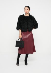Veste noire en peluche raccourcie, chemise noire, jupe midi bordeaux en cuir, sac à main noir avec un design clouté, collants noirs et chaussures à talons.