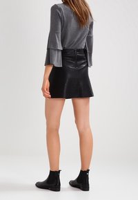 Grijze lange mouwen top met wijde manchetten, gecombineerd met een zwarte leren minirok met een ritssluiting aan de achterkant. Zwarte enkellaarsjes maken de look compleet.
