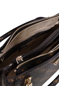 Sac fourre-tout noir avec un motif de logo doré, comportant plusieurs compartiments intérieurs et zippers. Texture en cuir lisse avec des accessoires en ton doré.