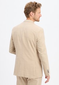 Beżowa marynarka z fakturowanej tkaniny, z jednym rozcięciem z tyłu i mankietami na dwa guziki. Slim fit z dopasowaną sylwetką.