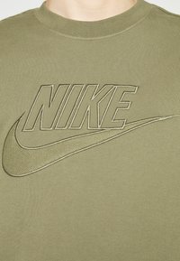 T-shirt en coton vert olive avec un logo Nike en relief dans une teinte plus claire, avec un col rond classique et une texture lisse.