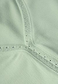 Tissu vert clair présentant une texture lisse, avec une couture décorative le long de la couture et de petits trous pour un détail supplémentaire.