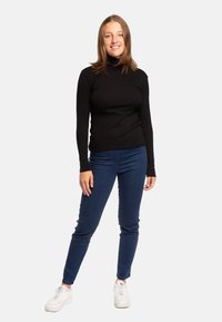 Pullover nero a maniche lunghe con collo alto abbinato a jeans skinny blu scuro e sneakers bianche. Materiale liscio con un design aderente. Aspetto semplice e pulito.