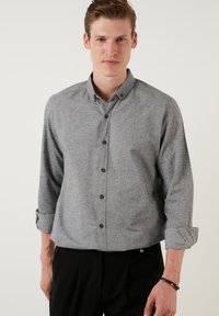 Grå skjorte med knaplukning i tekstureret stof, opsmøgte ærmer og rund krave. Har mørke knapper og en tætsiddende design.