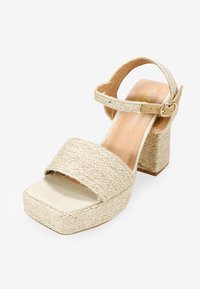 Sandalias de plataforma beige con detalles de paja trenzada, una tira delantera ancha, tira de tobillo con hebilla y un tacón bloque grueso.