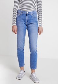 Světle modré džíny z denimu s rovným střihem, pěti kapsami, viditelným prošitím a mírně vybledlým vzhledem. Kombinovány s bílými teniskami.