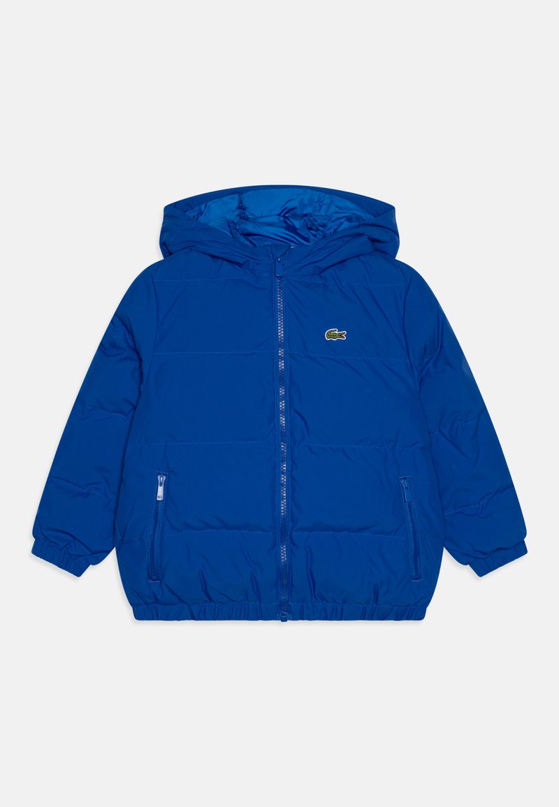 Modra napihljiva bunda s kapuco, z zadrgo spredaj, elastičnimi manšetami in stranskimi žepi. Ima majhen vezen logotip na levem prsnem delu.