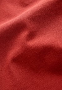 Tissu en coton dans une teinte rouge-brun chaud, présentant une texture lisse avec de légères rides, indiquant douceur et tombé.