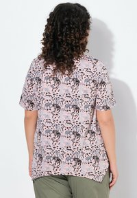 Camisa de manga corta rosa con un vistoso patrón de animales y árboles en negro y azul. Corte relajado con un dobladillo curvo y textura suave.