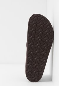 Brown rubber sandal sole with a textured, wave-patterned surface. Rounded shape and smooth edges, designed for comfort and grip.