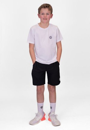 Camicia bianca a maniche corte con logo, abbinata a pantaloni corti neri. Sneakers con dettagli arancioni e calzini bianchi alla caviglia. Design atletico semplice.