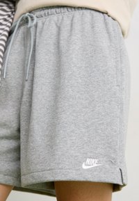 Shorts Nike griți, confecționați dintr-un amestec moale de bumbac, având un talie elastică cu șnur și un logo alb în partea stângă jos.