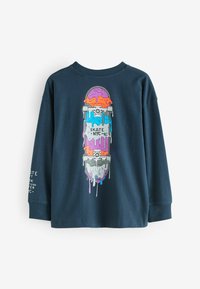 Kék hosszúujjú póló, élénk színekkel díszített skateboard grafikával, csepegő festékkel, kerek nyakkal és bordázott mandzsettával. Szöveg az ujjon.