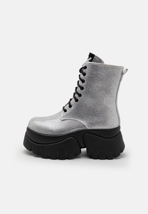 Hõbedased metallikust pahkluusaapad tekstuuriga pinnaga, musta tummi tallaga ja paeltega disainiga. Tagaküljel on lihtsaks selga tõmbamiseks venitusrihm.