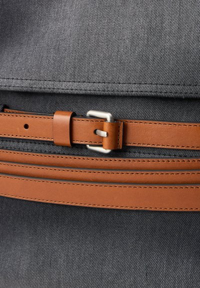 Torba kanvasowa z szarym tekstylnym korpusem, uzupełniona brązowym skórzanym paskiem i sprzączką, podkreślająca teksturowane wykończenie i czyste linie.