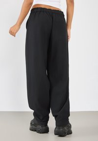 Sorte ribbede bukser med vid ben og elastisk talje, med sidelommer og en baglomme, parret med sorte chunky sneakers.