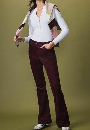 Haut blanc ajusté à manches longues avec patte de boutonnage associé à un pantalon évasé en velours côtelé bordeaux. Écharpe rayée multicolore drapée sur les épaules.