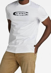 Camiseta blanca de G-Star con un estampado de logo ovalado negro en el pecho. De manga corta, hecha de algodón, con cuello redondo.