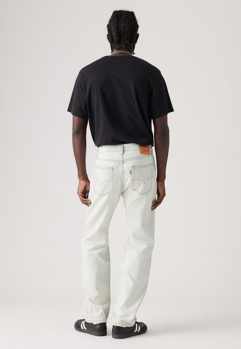 Camiseta negra de manga corta combinada con jeans de mezclilla claros. Los jeans tienen un corte recto y un parche de cuero en la parte trasera de la cintura.