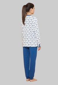 Maglietta a maniche lunghe bianca con motivo floreale blu, abbinata a pantaloni blu. La maglietta presenta dettagli in blu navy e polsini slim ai polsi e all'orlo.