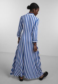 Robe longue rayée en bleu et blanc, avec un col et des manches trois-quarts. Jupe fluide avec des fentes latérales et des chaussures à plateforme noires.