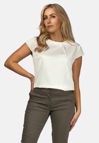 Biała bluzka z krótkim rękawem, o okrągłym dekolcie i subtelnymi plisami. Połączona z dopasowanymi oliwkowymi spodniami z kieszeniami.