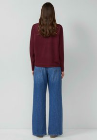 Brązowy prążkowany sweter z opuszczonymi ramionami w połączeniu z szerokimi dżinsami o kroju wide-leg w kolorze niebieskim. Dżinsy mają klasyczny fason z pięcioma kieszeniami.