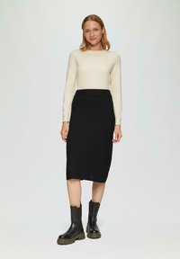 Brede crème lange mouw top, zwarte knielange getailleerde rok en zwarte enkellaarsjes met een stevige zool. Eenvoudig ontwerp, minimale details.
