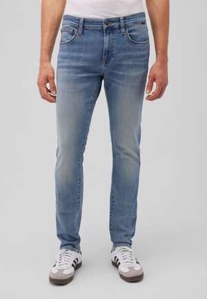 Hellblaue Denim-Jeans mit Slim-Fit, ausgestattet mit fünf Taschen und kontrastierenden Nähten. Kombiniert mit weißen Sportschuhen.