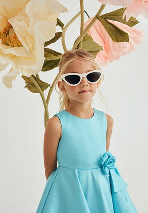 Abito azzurro chiaro con un corsetto aderente e una gonna svasata, con un accento floreale. Il bambino indossa occhiali da sole bianchi a forma di occhio di gatto. Lo sfondo include grandi fiori.