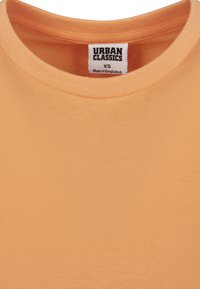 T-shirt orange à manches courtes avec un col rond, fabriqué en coton doux. L'étiquette indique "URBAN CLASSICS" avec la taille XS.