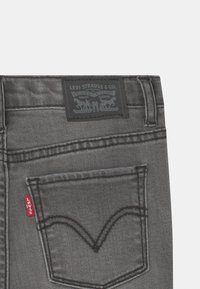 Jeans grises de Levi's con un acabado de denim texturizado, costuras doradas, etiqueta roja distintiva y un parche de cuero negro con la marca en la cintura.