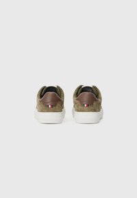 Brown suede sneakers featuring a white rubber sole, rounded heel, and a small accent with red, white, and blue stripes at the back.