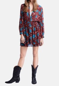 Robe florale à manches longues sur fond bordeaux avec des roses bleues. Taille élastique, coupe ample et texture superposée. Assortie à des bottes de cow-boy noires.