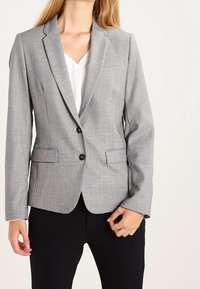 Gray tailored blazer with a notch lapel, two front pockets, and two buttons. Worn over a white top, paired with black slacks. Smooth texture.