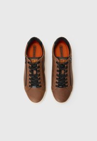 Brown textured sneakers with black laces and a side zipper. Interior features bright orange lining and a logo tag near the laces.
