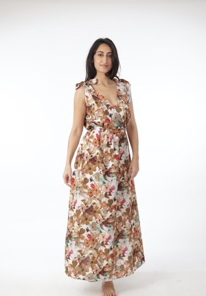 Kvinde iført ærmeløs blomster maxi-kjole i brune, hvide og lyserøde nuancer, stående foran en ensfarvet hvid baggrund.