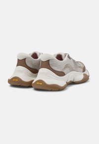 Para beżowo-brązowych masywnych sneakersów z siatkową tkaniną, grubymi białymi podeszwami i logo Vibram na zewnętrznych piętach, widzianych od tyłu.