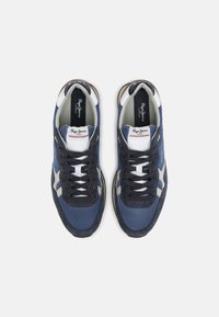 Námořnické modré sportovní tenisky s texturami z prodyšné tkaniny a semiše, bílými akcenty a tmavými tkaničkami. Obsahují logo na jazyku a na boku.