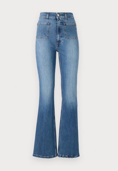 Dzwony z niebieskiego denimu z wysokim stanem, z dwoma tylnymi kieszeniami i wyblakłym wykończeniem. Doły spodni są obszyte subtelnym wzorem.