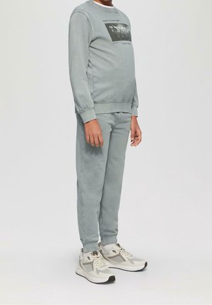 Light gray sweatshirt and matching sweatpants in soft fabric, featuring a graphic print on the shirt. Paired with beige and gray athletic sneakers.