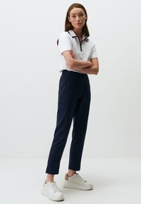 Witte poloshirt met zwarte kraag, marineblauwe op maat gemaakte broek en witte sneakers met gouden accenten. Gladde stof, aansluitend ontwerp en klassieke silhouet.