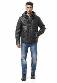 Schwarze Lederjacke mit gesteppten Schulterpolstern, Reißverschlusstaschen und grauer Kapuzenjacke darunter. Blaue Jeans und schwarze Stiefel vervollständigen das Outfit.
