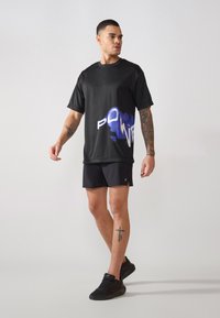 Schwarzes T-Shirt mit kurzen Ärmeln und blau-weißer "POWER" Grafik, kombiniert mit schwarzen Shorts und schwarzen Sport Schuhen.