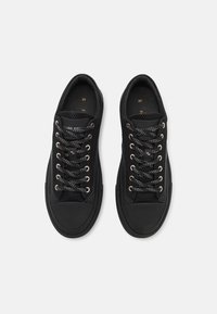 Černé tenisky z síťoviny a kaučuku, s kulatými tkaničkami, kovovými průchodkami a texturovanou špičkou s hladkým povrchem.