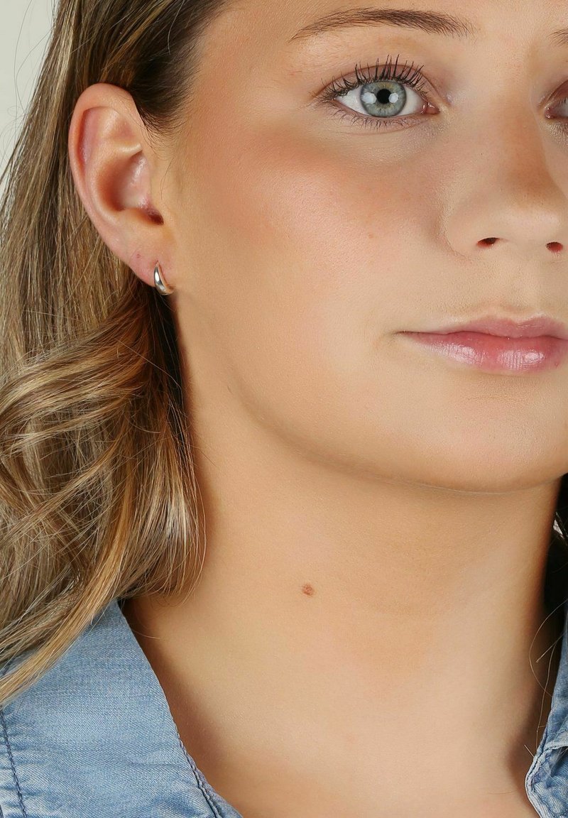 Silver hoopörhänge som visas på en models öra. Designen har en slät, glänsande yta med en enkel, böjd form.