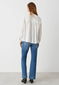 Top lungo leggero color avorio con maniche, dotato di una parte posteriore arricciata, abbinato a jeans in denim blu a zampa d'elefante e stivaletti neri alla caviglia. Look semplice e informale.