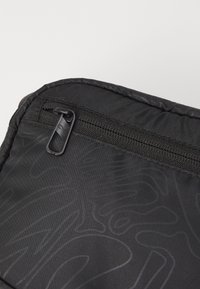 Svart tygväska med ett zippered fack och subtilt präglad mönster. Har en texturerad yta och en liten dragflik på dragkedjan.